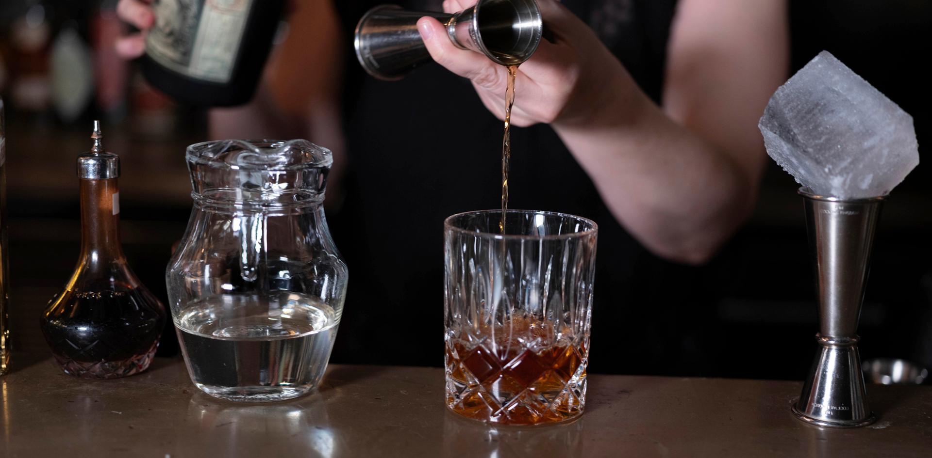 Person pouring drinks into a glass while making a cocktail