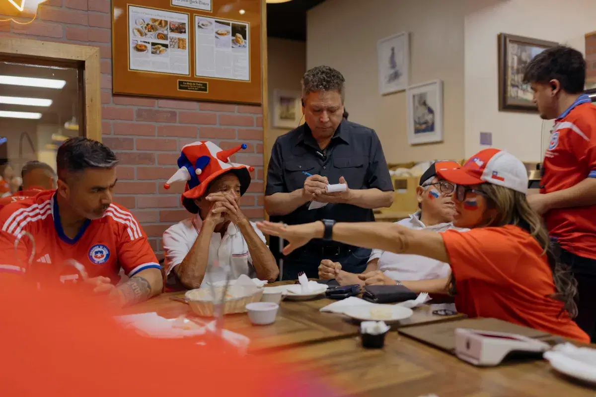 The owner of La Roja de Todos takes food and drink orders from a table. 