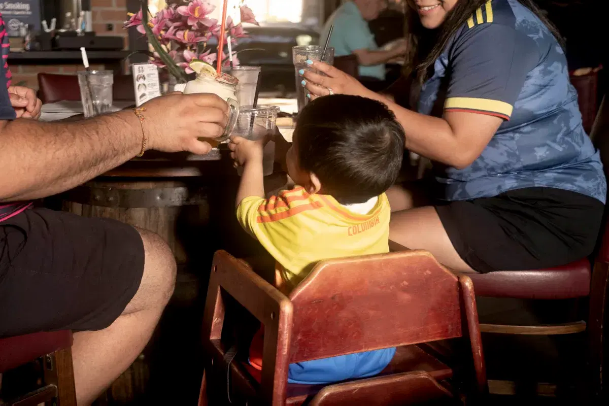 A young kid and family wearing Colombia soccer shirts toast while watching the Colombia vs Costa Rica game at Bar 43 in Queens. 