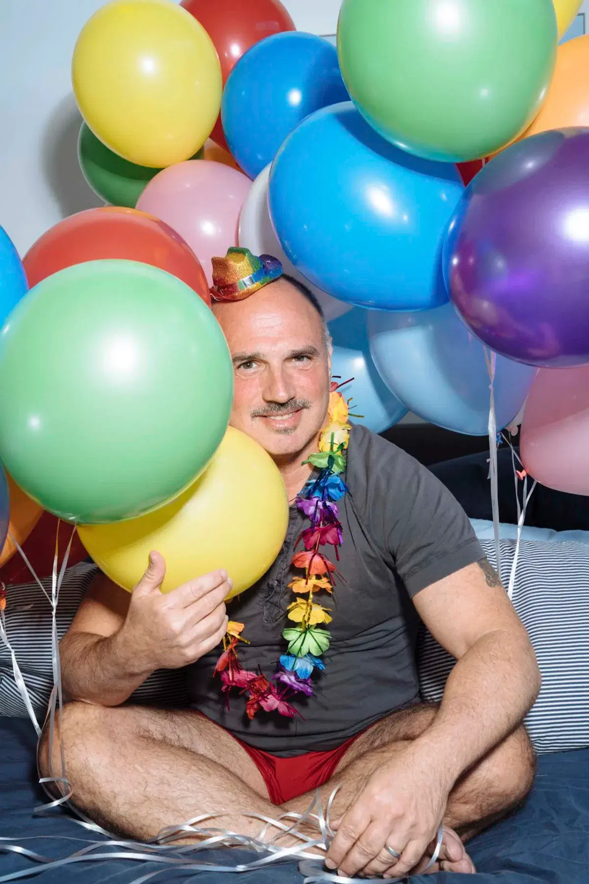 Person wearing colorful hat and necklace surrounded by colorful balloons