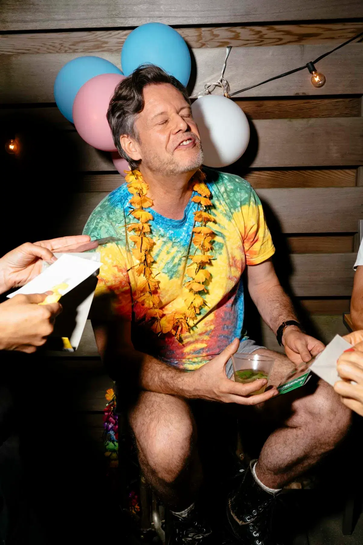 Person wearing colorful shirt and necklace surrounded by balloons