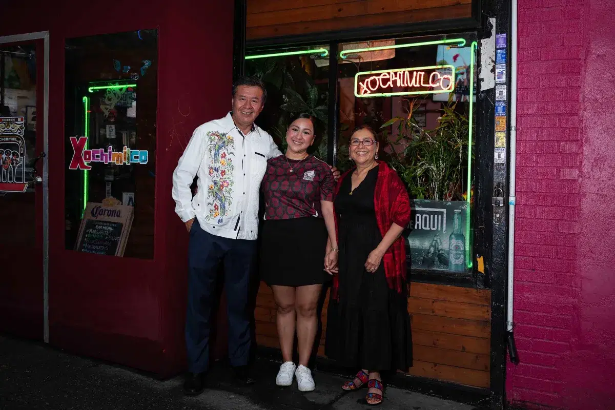 The owners of Xochimilco and their daughter pose to the camera in the exterior of their restaurant 