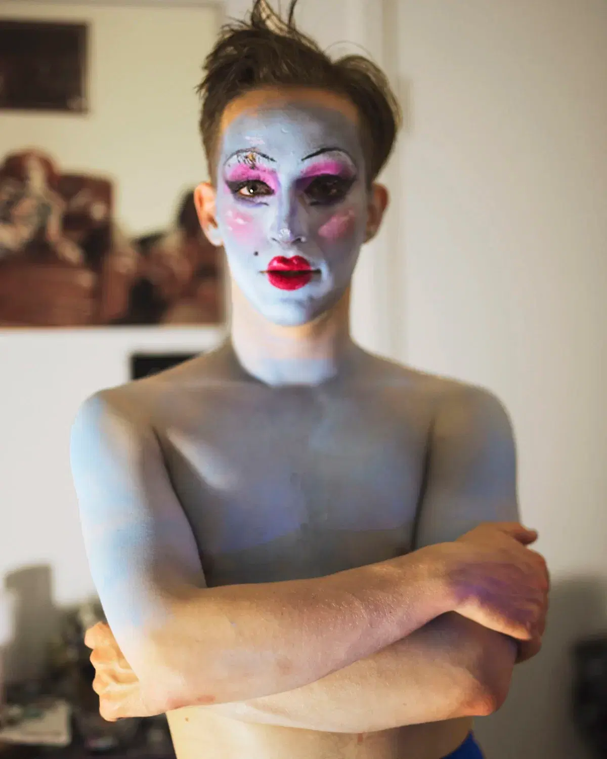 a man with his arms crosse wearing performance makeup